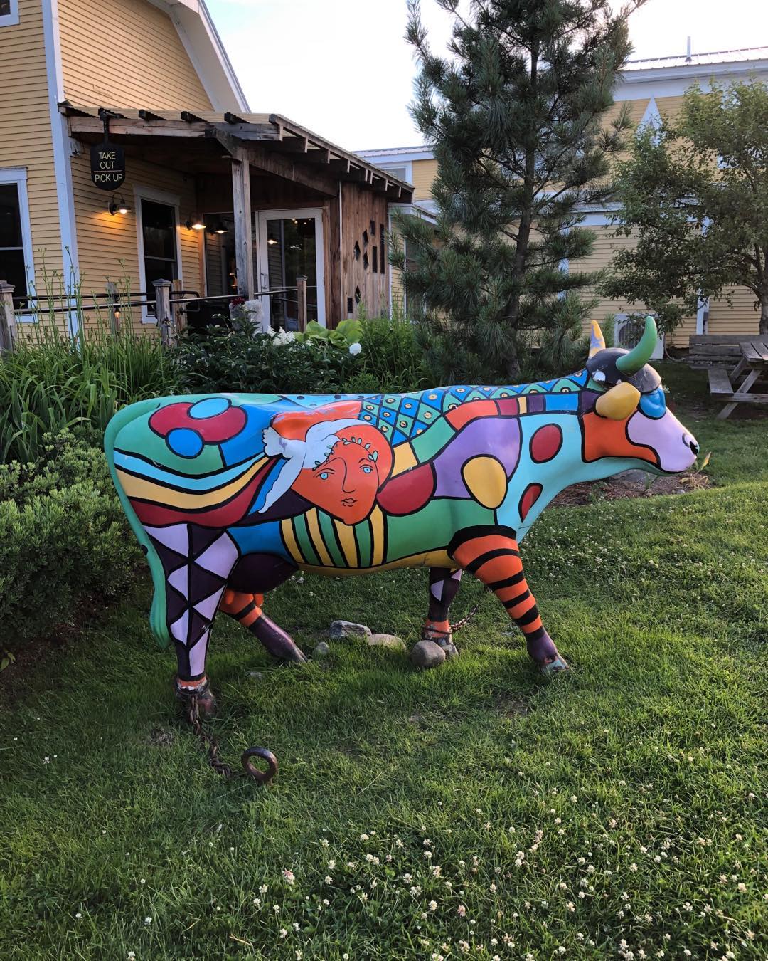 A brightly painted cow sculpture in front of a yellow shop